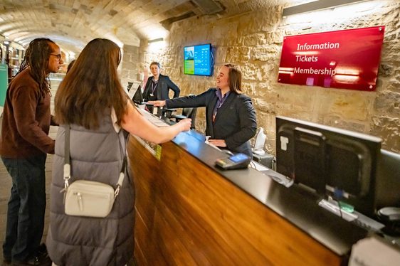 A member of museum staff standing behind a desk pointing handing a paper map to a family.