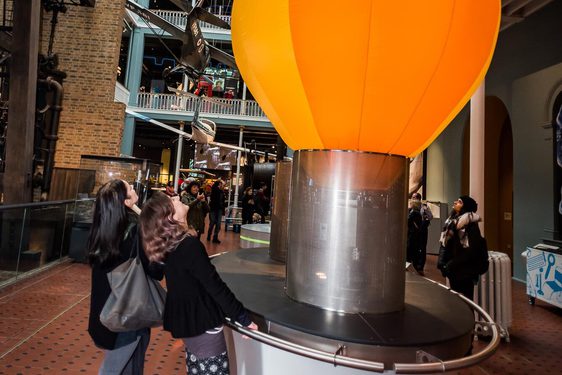 Two visitors watching hot air balloons ascend in a museum gallery.