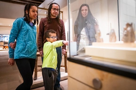 A family looking at stone chess pieces in a museum case.