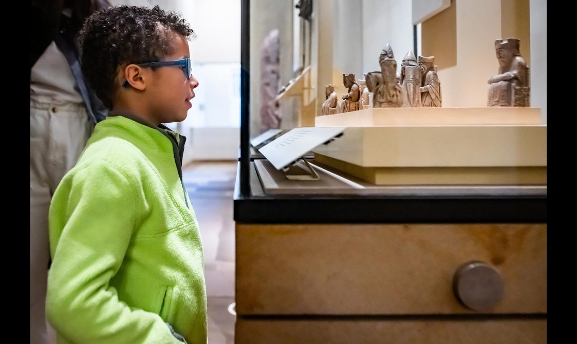 A child looking at small stone chess pieces in a glass museum case.