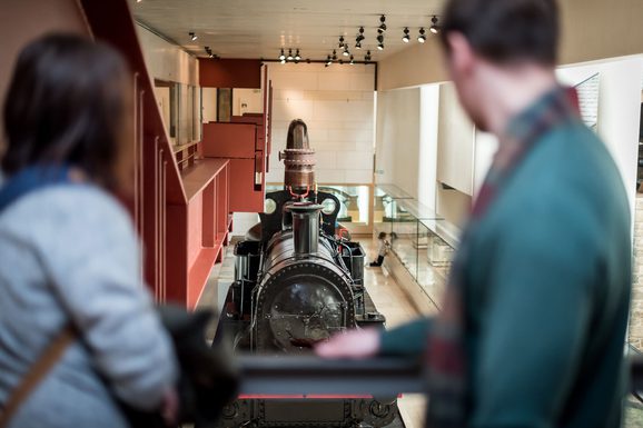 Two visitors looking down at a steam locomotive in a large museum gallery.