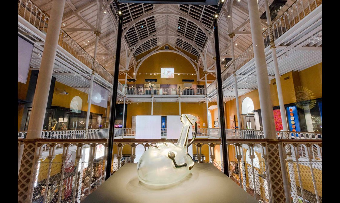 Close-up of a circular glass jug within a glass museum case.