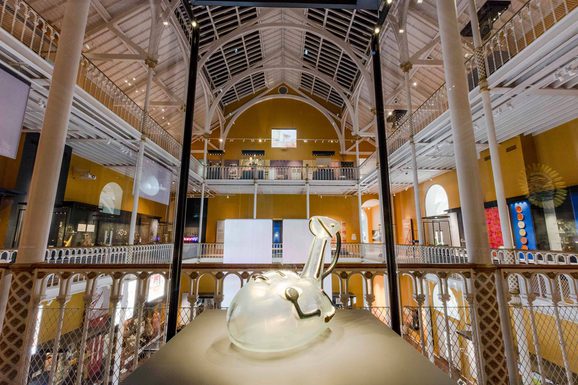Close-up of a circular glass jug within a glass museum case.
