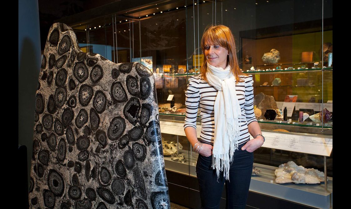 A museum visitor looking at a tall flat rock covered in black discs.
