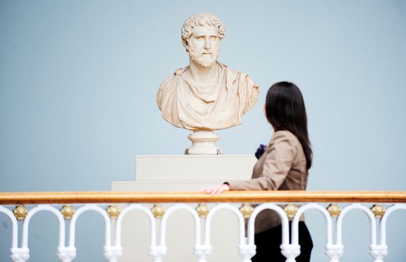 A visitor looks at a bust sculpture of a Roman figure.