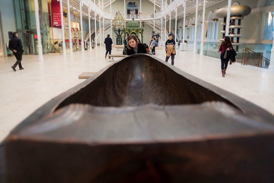 Close up of a visitor looking at a long wooden feast bowl in a museum gallery.