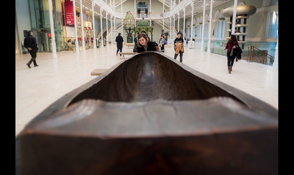 Close up of a visitor looking at a long wooden feast bowl in a museum gallery.