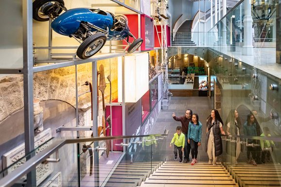 A family walking up a staircase looking at objects mounted on a museum gallery wall.