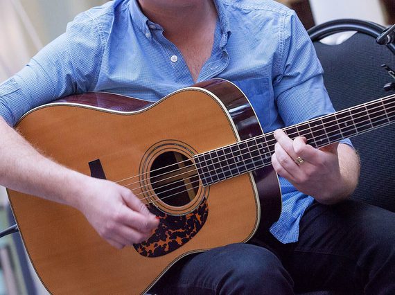 Close up of a musician in a blue shirt playing a guitar.