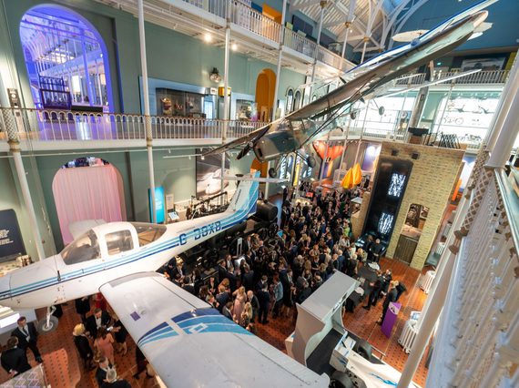 People at a drinks reception in a multi-level museum gallery. There are different aircraft suspended from the ceiling.