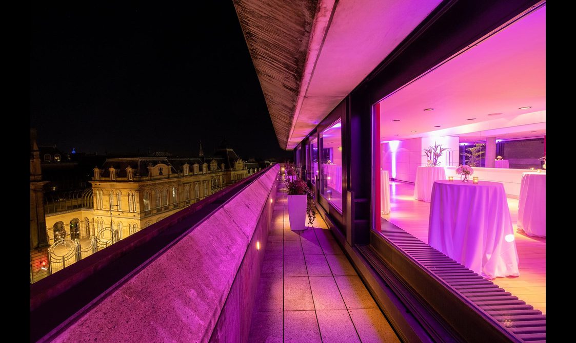 A rooftop space illuminated with pink light, overlooking the city of Edinburgh.