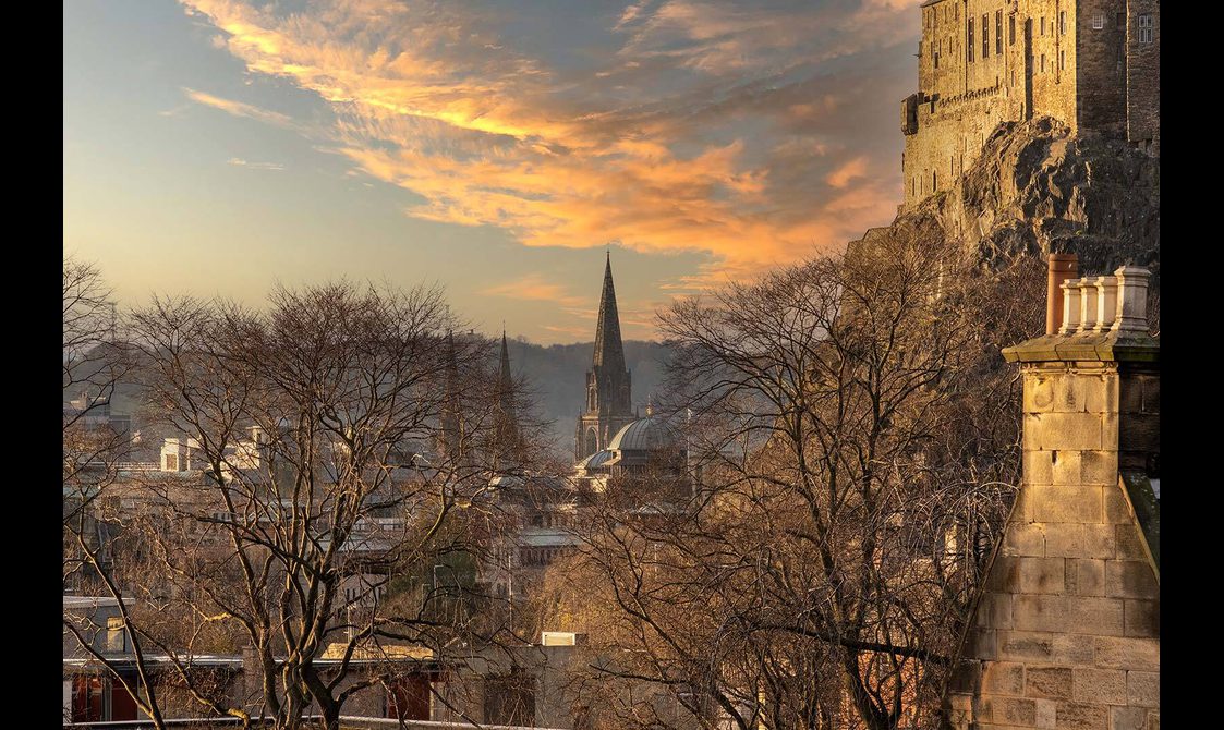 Rooftop view of the city of Edinburgh. In the distance are church steeples and Edinburgh castle is to the right.