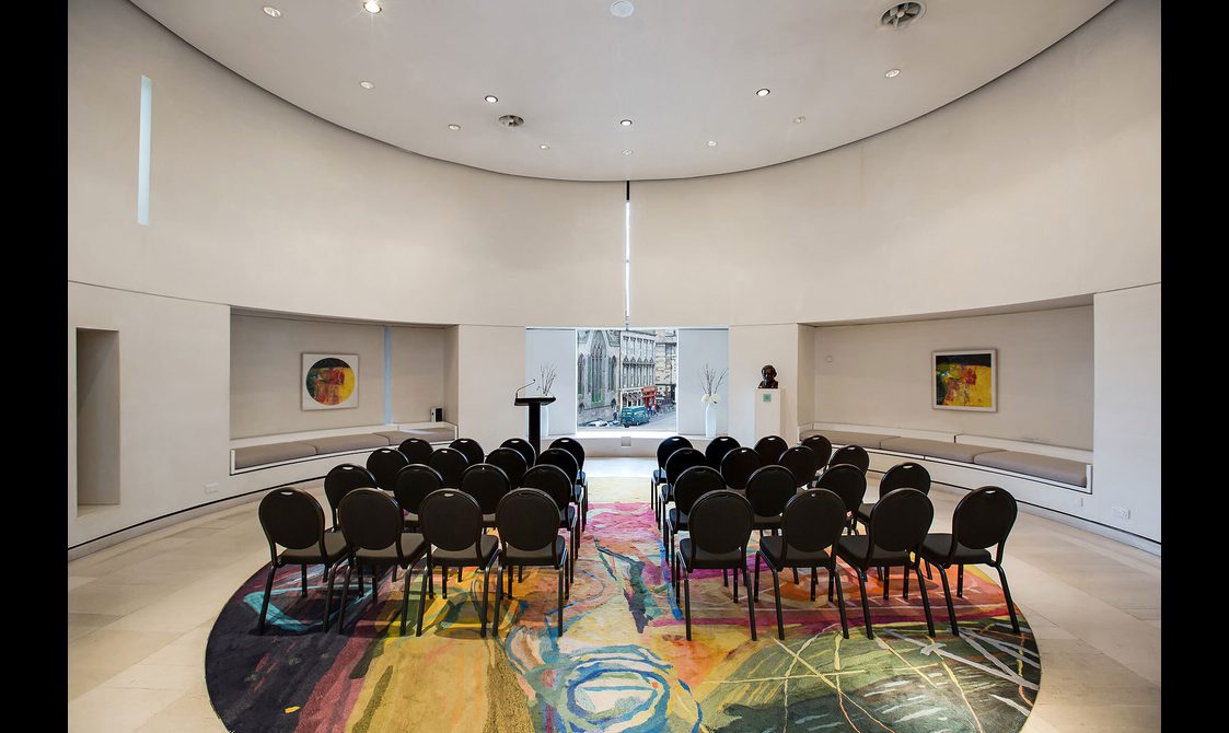 Rows of chairs set up in a white cylindrical room. There is a podium in from of a window looking out onto the streets of Edinburgh.