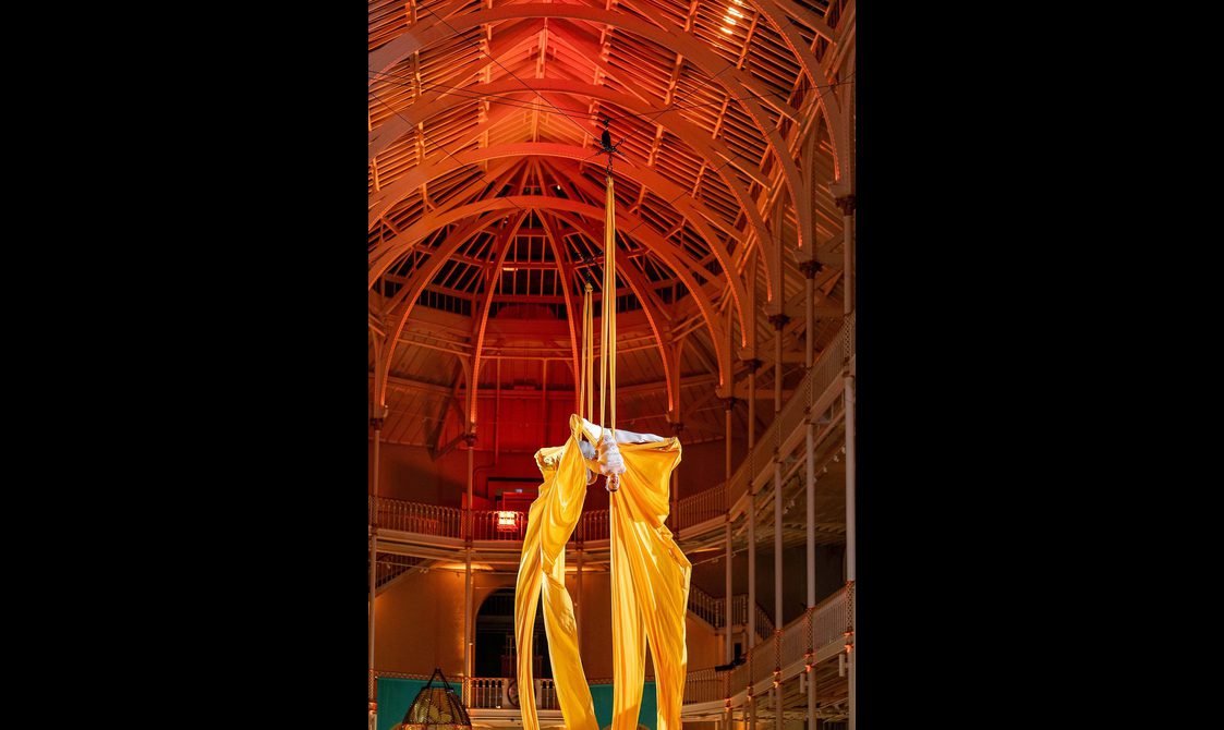 Two aerial artists suspended from a gallery ceiling by yellow cloth.
