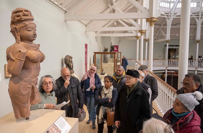 A group of people stand observing a statue mounted on a plinth