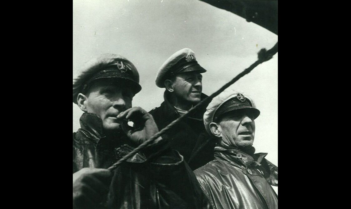 A black and white photograph of three men wearing jackets and sailor hats gazing outward.