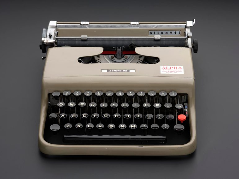 A typewriter with black keys and a beige shell