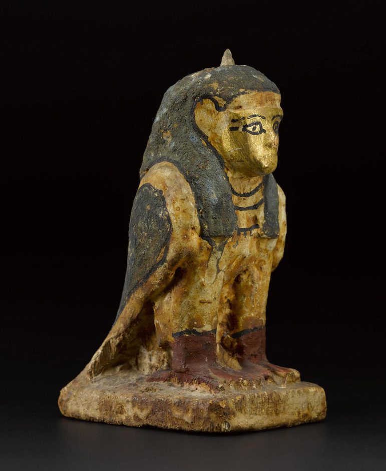An Egyptian statue of a creature with the body of a falcon and the head of a human painted gold, blue, and red.