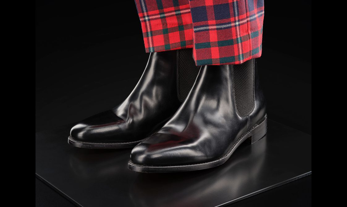 Men's black leather chelsea boots with red tartan trousers.