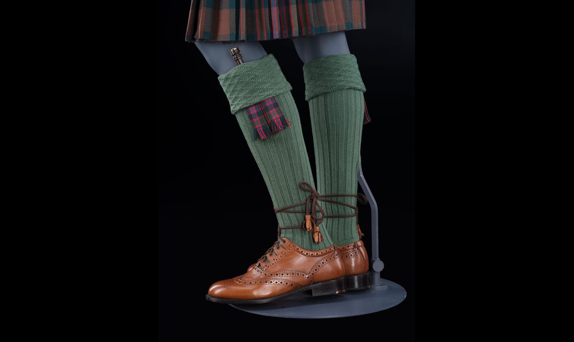 A mannequin wearing knee high green socks with a small knife tucked into the sock and brown leather shoes