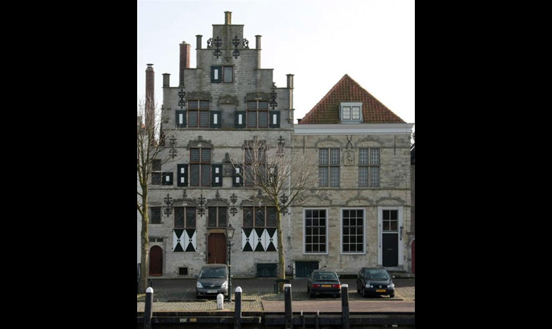 Two terraced houses, one with pitched roof, and the other one with a stair shaped roof facade. Three cars parked in front.