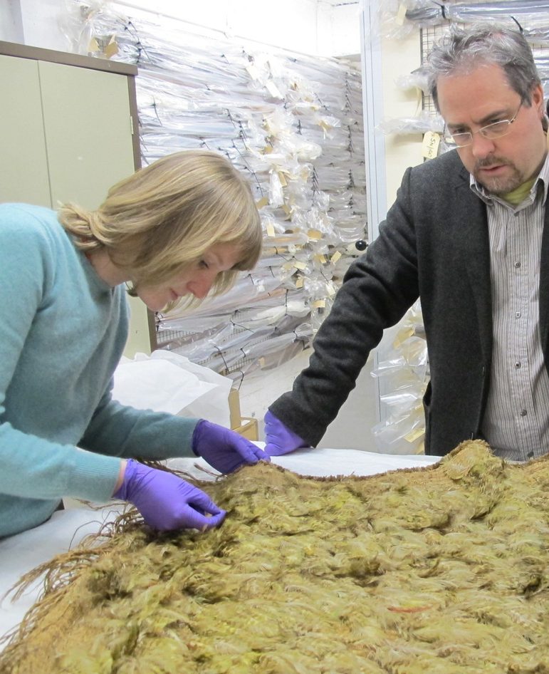 Two people examine a cloak made out of pale yellow feathers