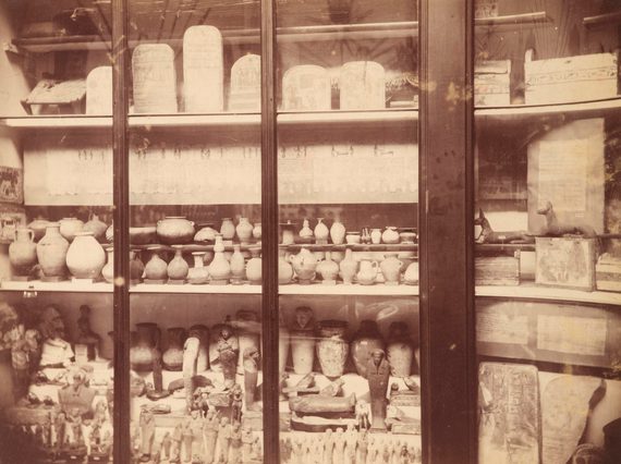 Shelves of a large group of old pottery behind a glass cabinet door.