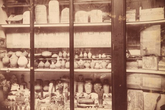 Shelves of a large group of old pottery behind a glass cabinet door.