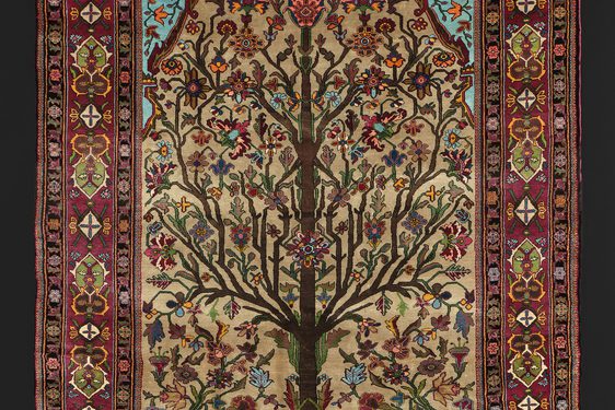 Silk rug depicting an angular tree with branches full of flowers. It is surrounded by a red border with various embellishments.