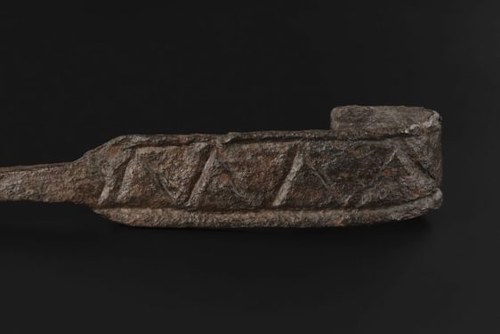 Closeup of a zigzag pattern forming bordered triangles on the flat surface of the hooked end of an iron cruik.