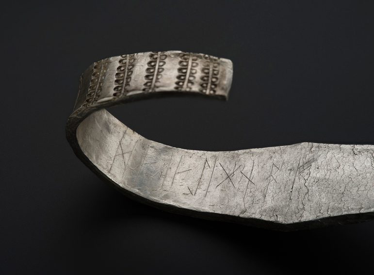 The largest silver arm ring, which has a curved end to it. On the inside, you can see a runic inscription.