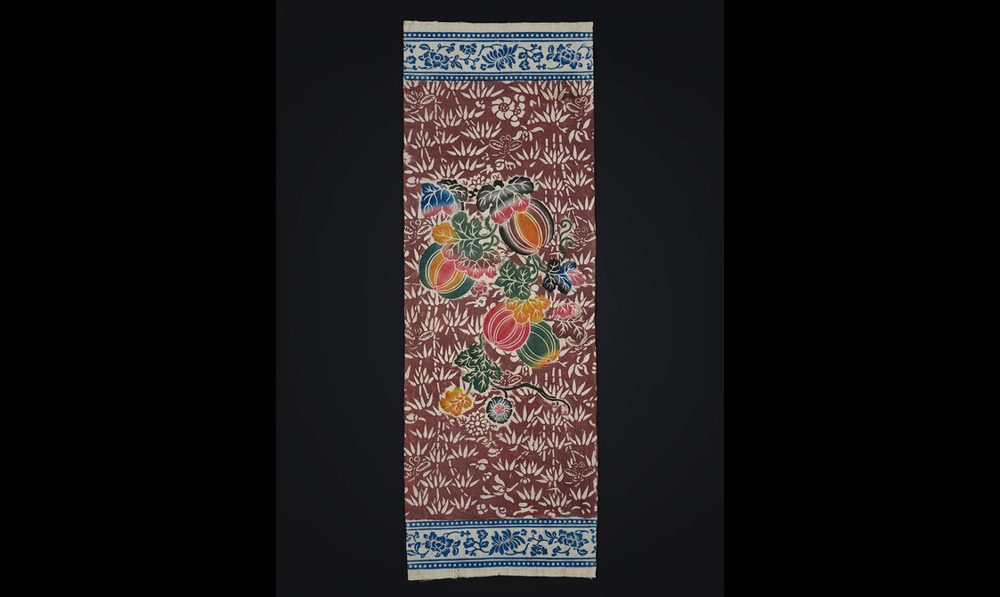 Cotton printed with intricate blue and red pattern with colourful green pink and orange fruits and vegetables.