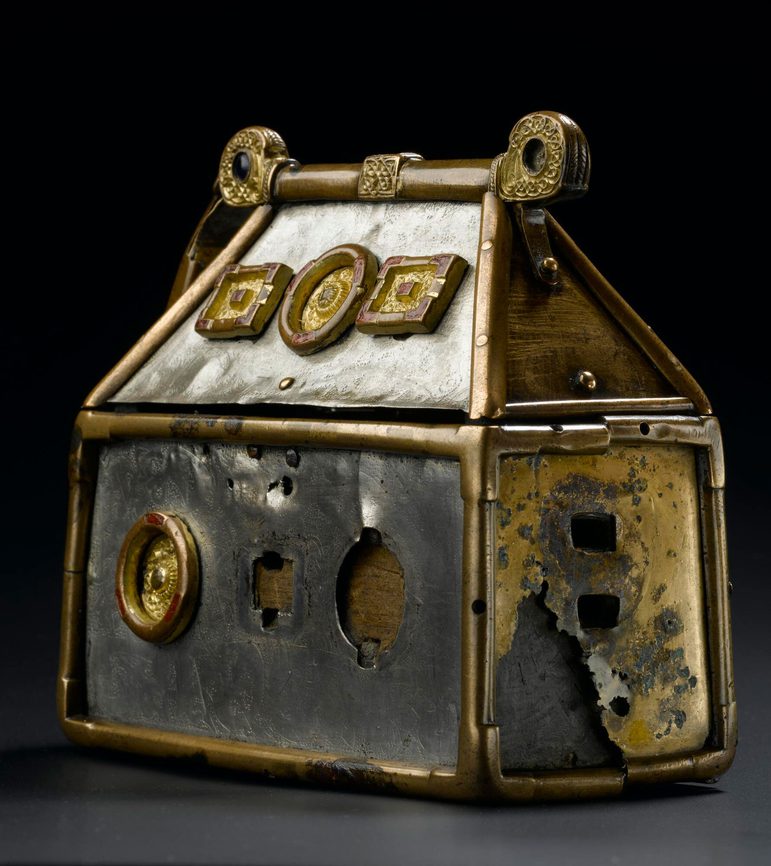 A small silver box with gold metalwork on the edges. In view is a damaged copper side plate revealing wood underneath.