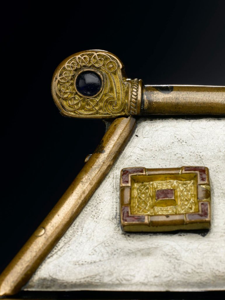Close up of the roof of a silver box with gold metalwork on the edges. In focus is a spherical end of the bar of the roof, which has interlacing patterns that form a hidden cross.