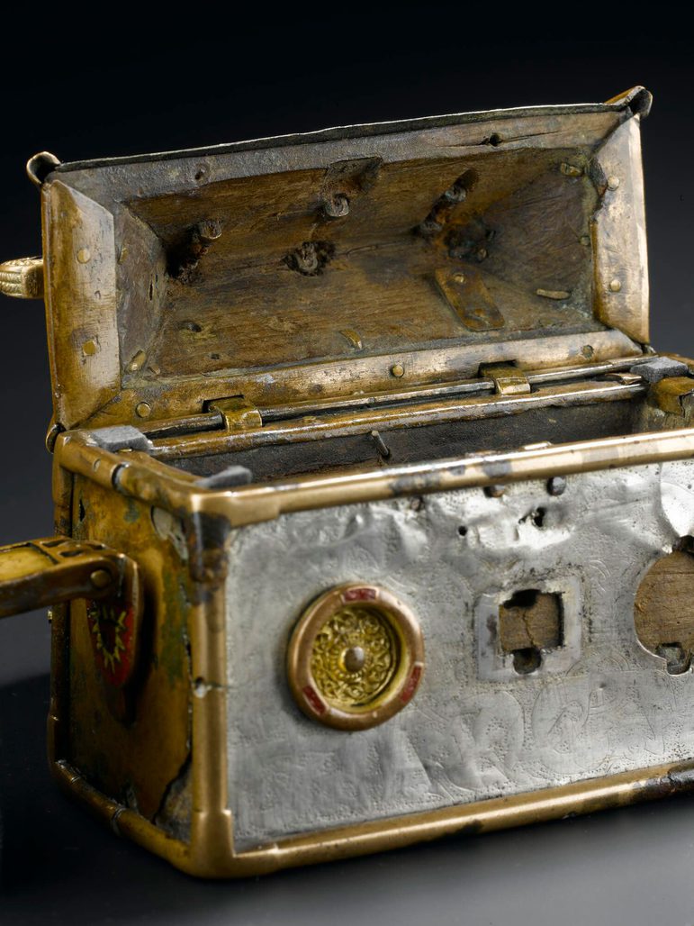 A small silver box with gold metalwork on the edges. The lid of the box is open revealing the inside.