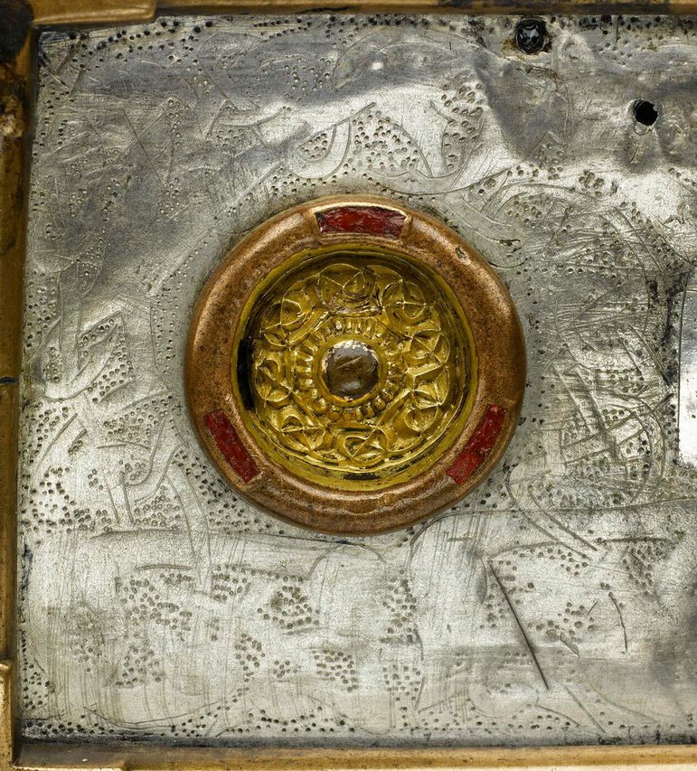 Close up view of a gold circular mount on a silver box. There are interlacing designs on the box.