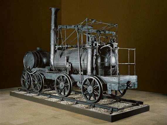 A large black locomotive from the 19th century on display against a brown background.