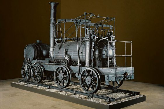 A large black locomotive from the 19th century on display against a brown background.