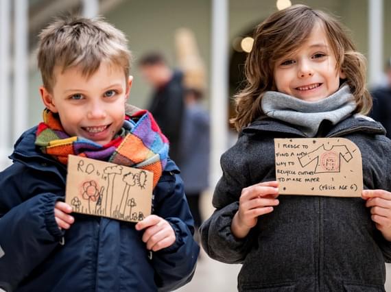 Two young people are holding up climate pledges and smiling at the camera.