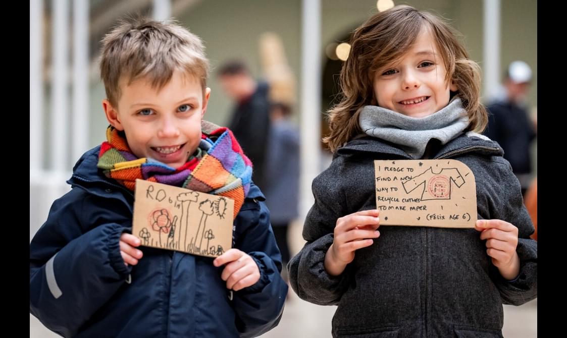 Two young people are holding up climate pledges and smiling at the camera.