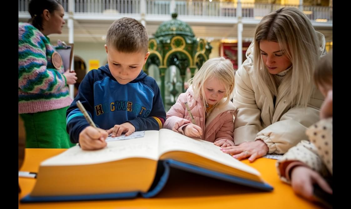Young people and their carer are writing in a very large book.