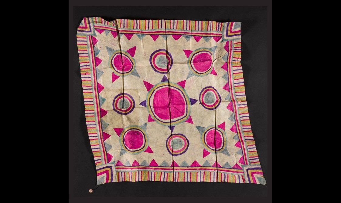 A pink, white, and grey square piece of textile laid flat with a striped border and circular pattern.