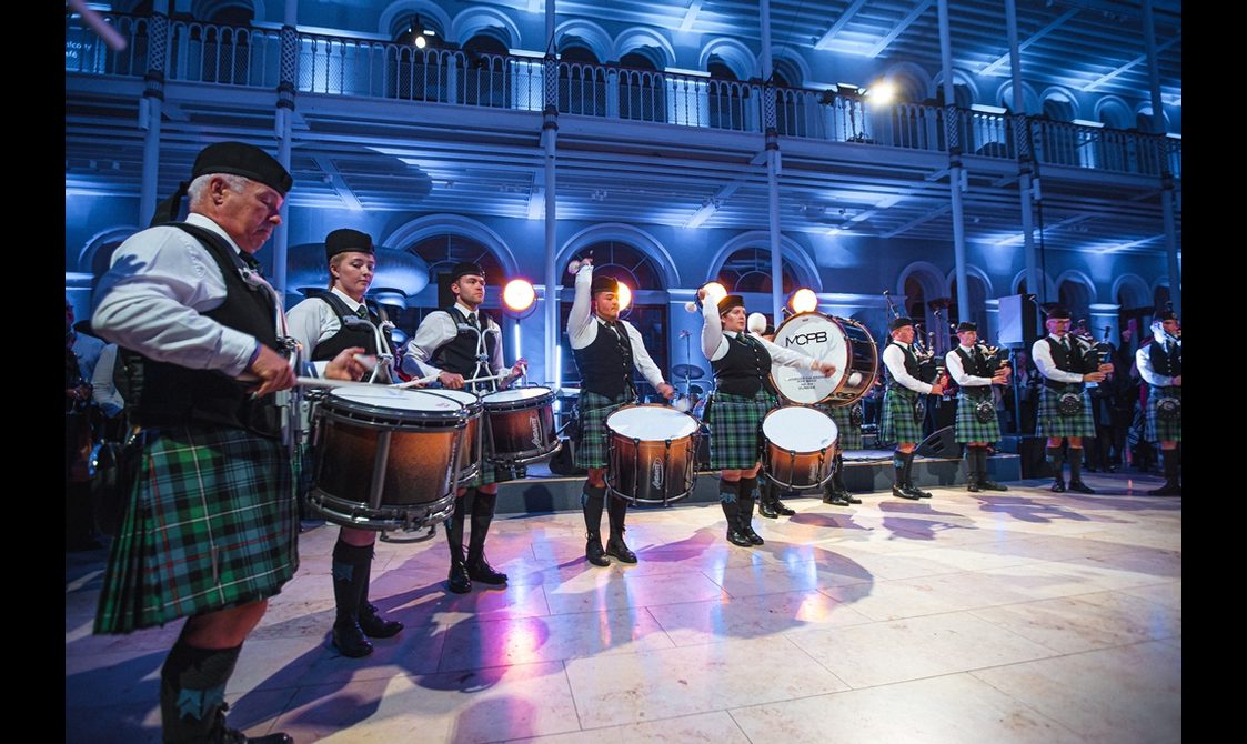 A pipe band performing in a museum gallery. The band members are wearing traditional Scottish dress.