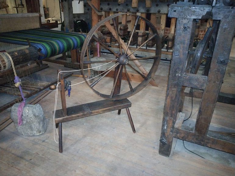 An old wooden spinning wheel in a weaving studio with various wooden looms