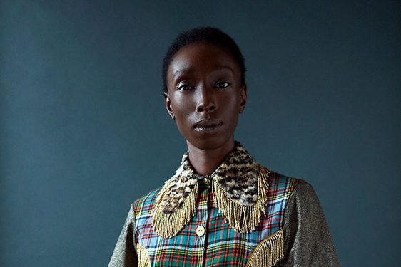 A woman poses in a patterned shirt and striped trousers