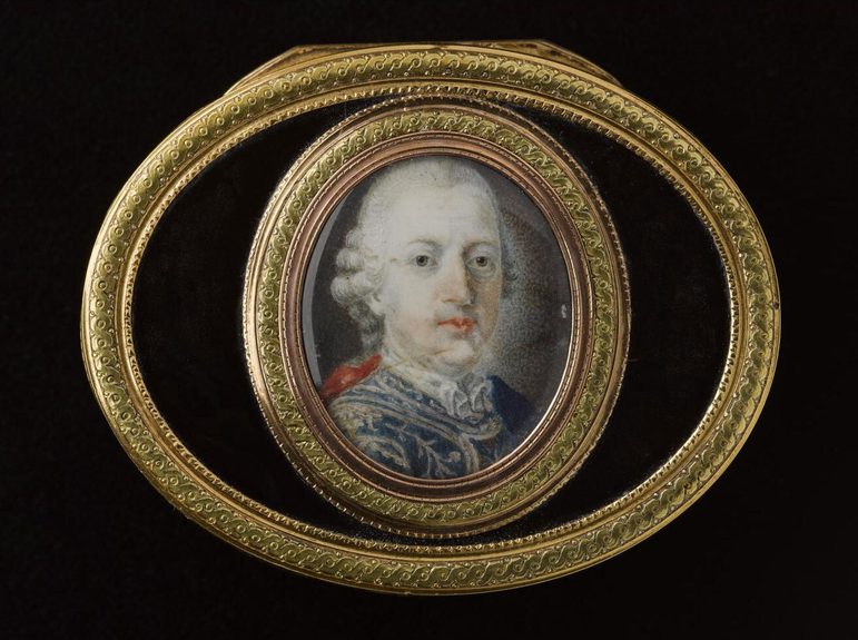 Detail of the snuffbox lid, with two oval shapes: the outer oval horizontal, the center one vertical. The edges decorated with gilded pattern. The center oval shows a portrait of a man wearing a white ruffle wig and an ornate blue jacket.
