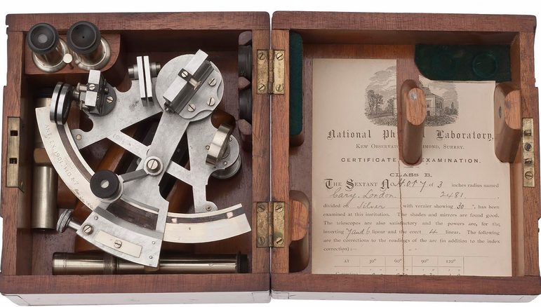 Open wooden box with triangular metal tool in one side and a printed sheet of paper in the lid.