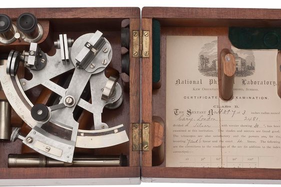 Open wooden box with triangular metal tool in one side and a printed sheet of paper in the lid.