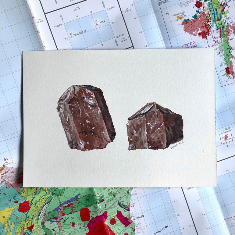 An illustration of reddish minerals on a white piece of paper. The illustration is photographed against a geological map of Scotland.