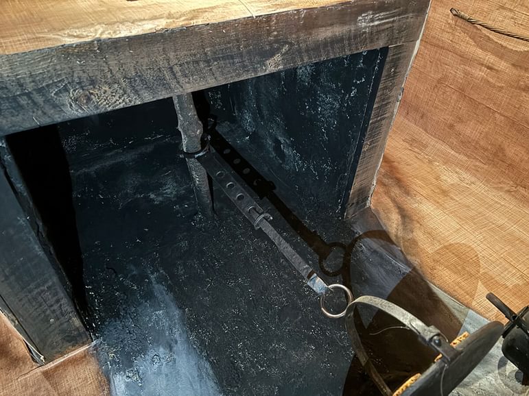 A beam situated in the lower part of a chimney, from which hangs a cruik and a pot